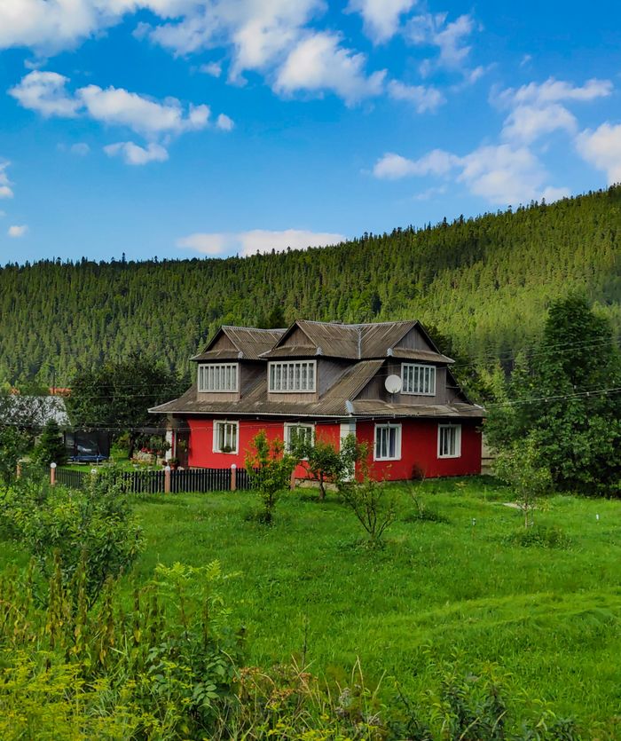 Mastering the First Impression: Your intriguing post title goes here A picturesque red house surrounded by lush greenery and rolling hills under a bright sky.